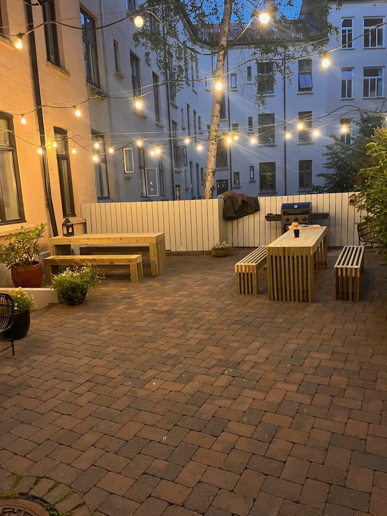 Uteplass med håndlagde bord og benker i tre, opplyst av lyslenker