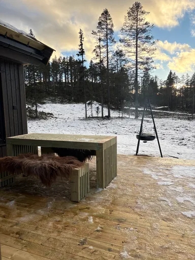 Bord og benk med saueskinn på vinterterrasse ved hytte