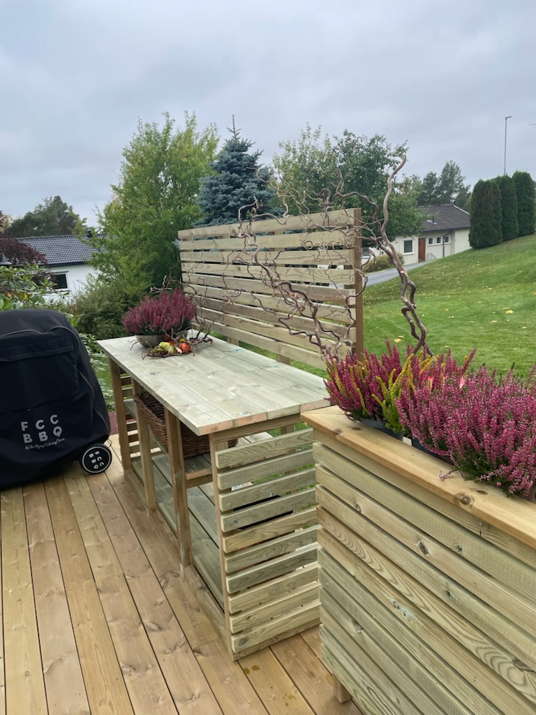 Utekjøkken i tre med benk og spiler ved blomsterkasse på terrassen