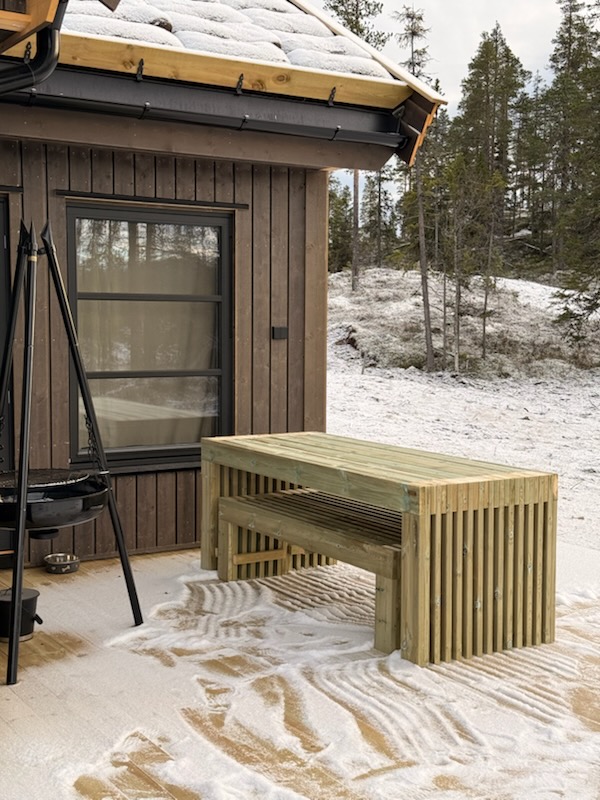Spilebord og benk utenfor hyttevindu med bålpanne