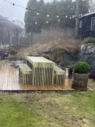 Bordgruppe i tre på terrasse under lyslenker i hagen